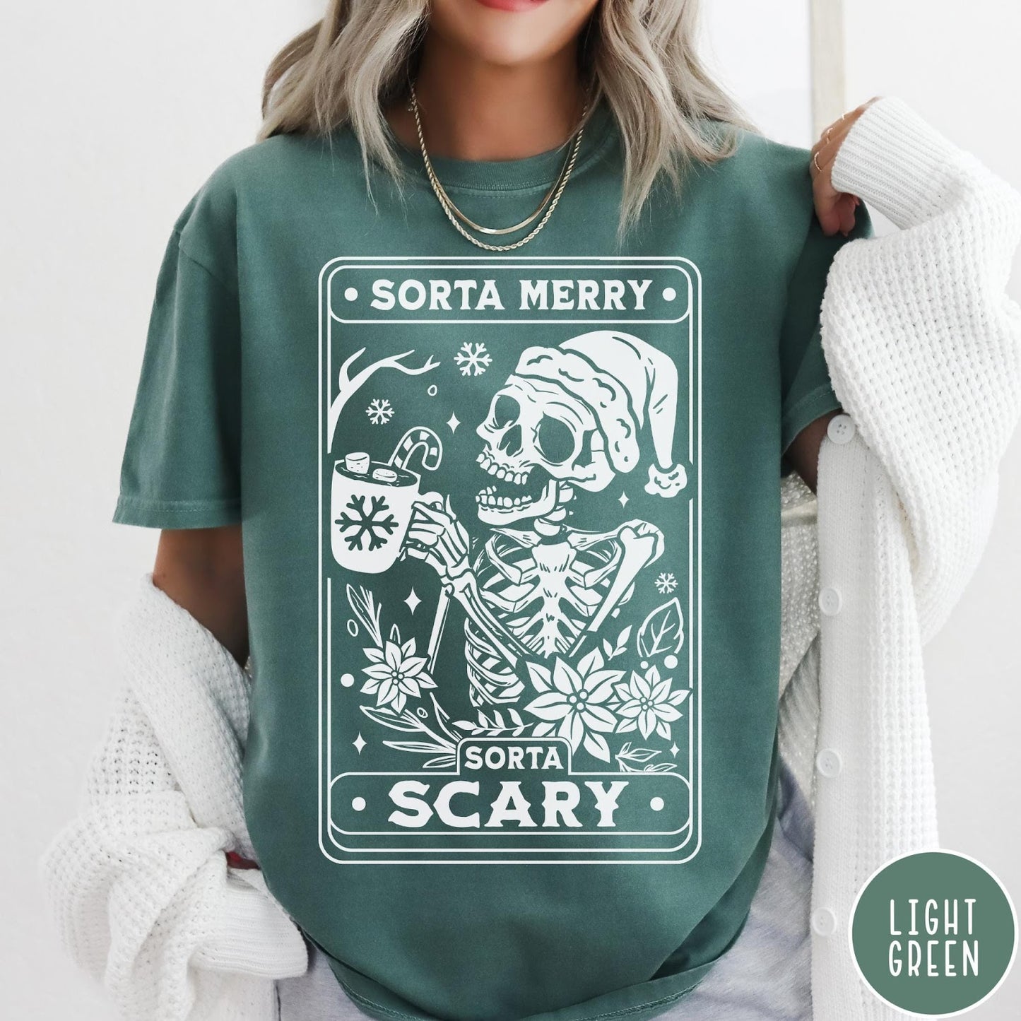 Comfort Colors tee in Light Green featuring graphic design of a skeleton in a Santa hat holding cocoa