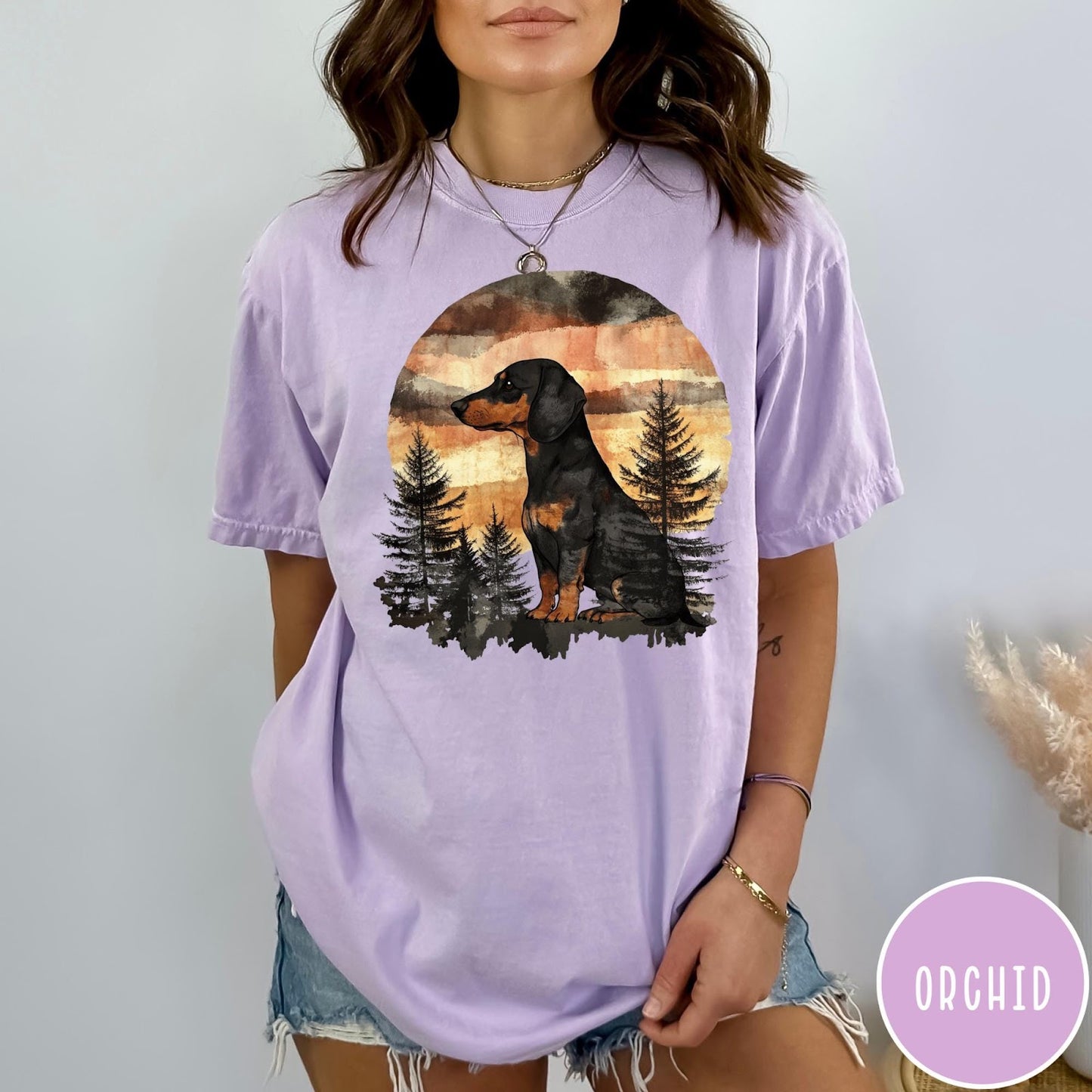 Comfort Colors tee in Orchid featuring vintage style graphic of a dachshund sitting in a forest sunset