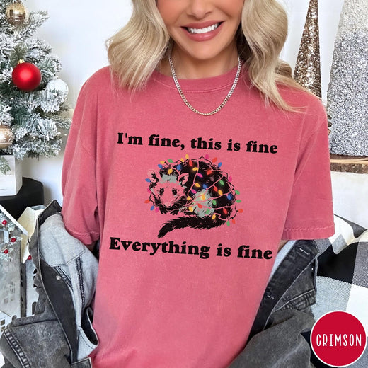 Comfort Colors tee in Crimson featuring graphic illustration of an opossum tangled in colorful Christmas lights