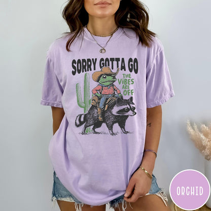 Comfort Colors tee in Orchid featuring western graphic of a cowboy frog riding a raccoon with cactus