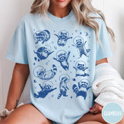Comfort Colors tee in Chambray featuring whimsical space design with multiple raccoons wearing glass astronaut helmets and stars