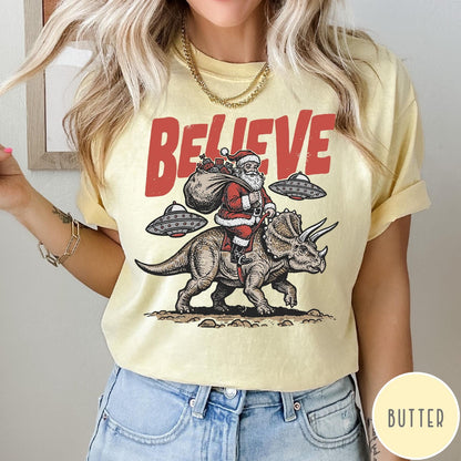 Comfort Colors tee in Butter featuring graphic illustration of Santa riding a dinosaur with flying saucers above