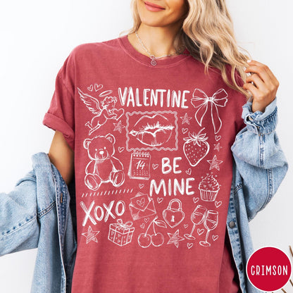Comfort Colors tee in Crimson featuring sketch style Valentine's Day collage graphic with cupid, bear, and hearts