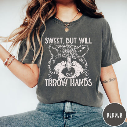 Comfort Colors tee in Pepper featuring graphic style raccoon illustration with text Sweet But Will Throw Hands