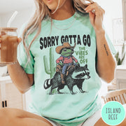 Comfort Colors tee in Island Reef featuring western graphic of a cowboy frog riding a raccoon with cactus