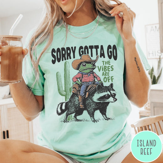 Comfort Colors tee in Island Reef featuring western graphic of a cowboy frog riding a raccoon with cactus