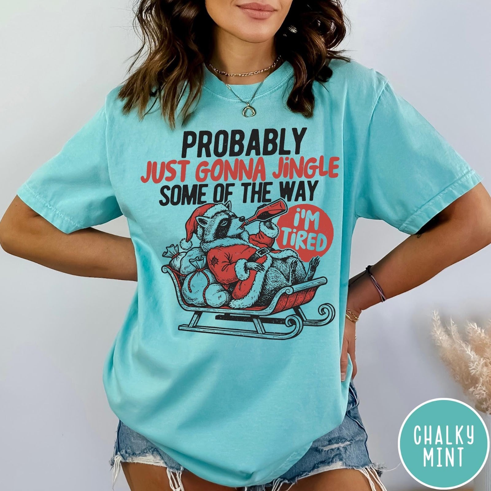 Comfort Colors tee in Chalky Mint featuring festive raccoon graphic in a sleigh with holiday text design