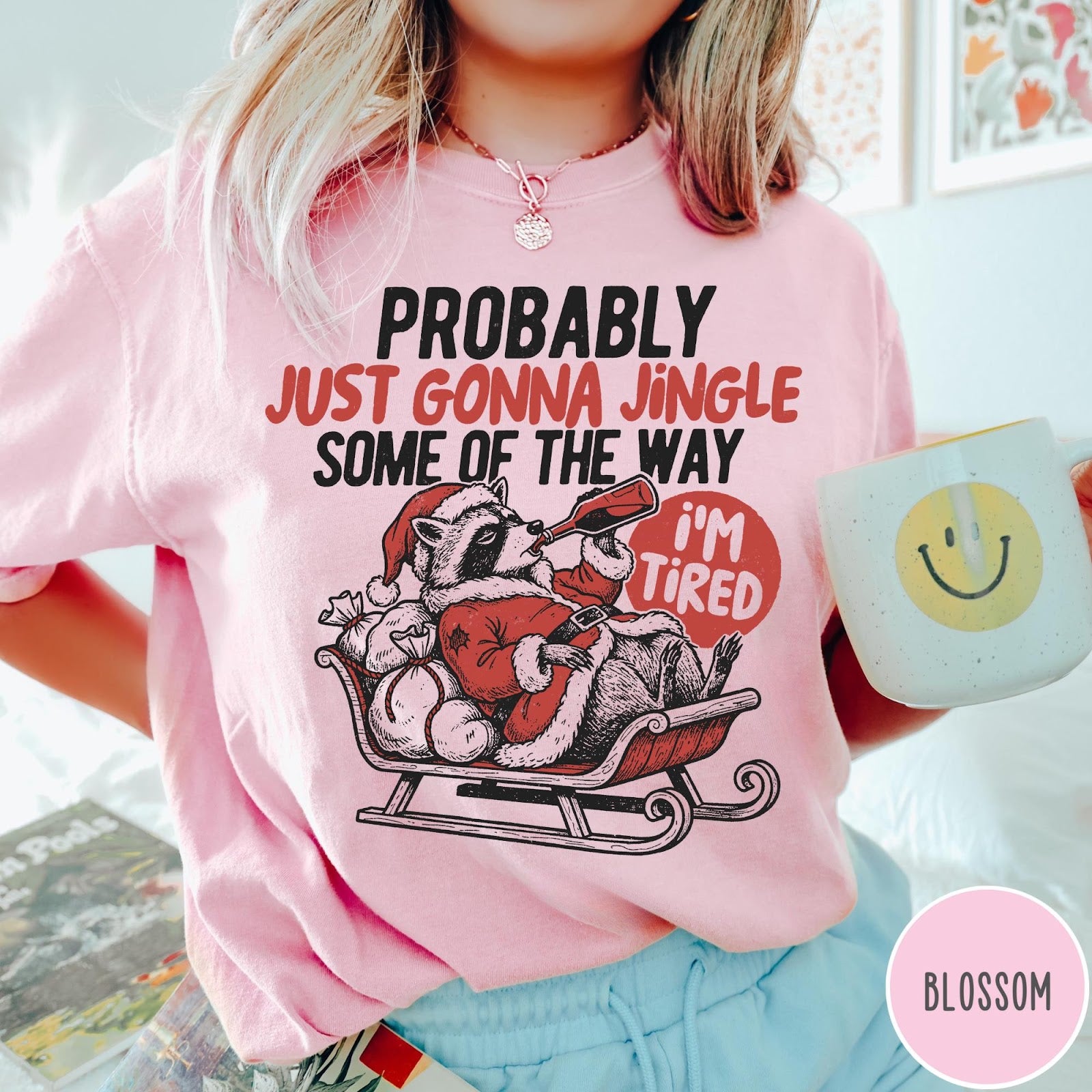 Comfort Colors tee in Blossom featuring vintage style graphic of a tired raccoon in a Santa sleigh