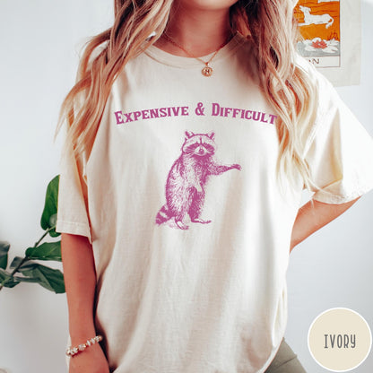 Comfort Colors tee in Ivory featuring vintage style graphic of a standing raccoon with text Expensive and Difficult