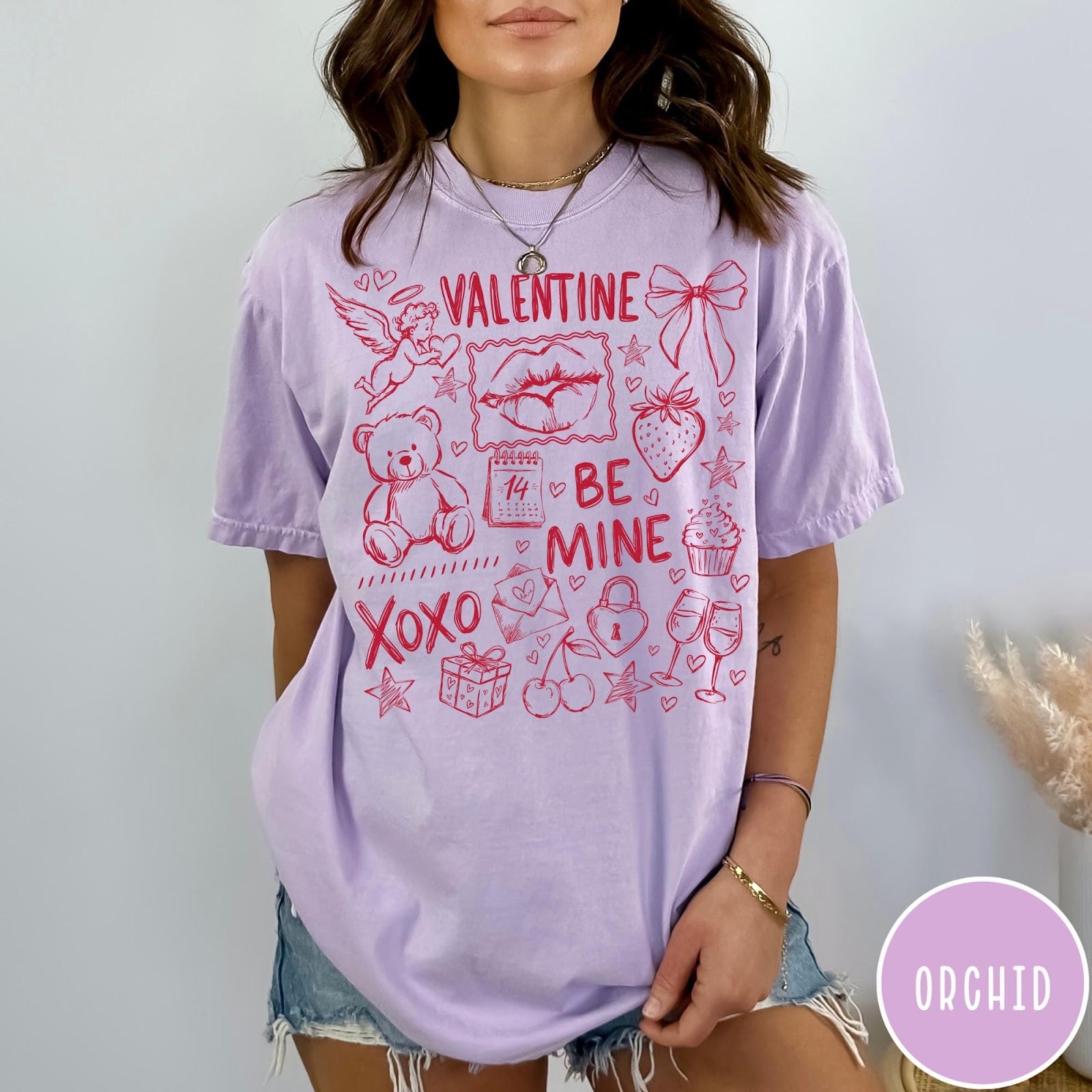 Comfort Colors tee in Orchid featuring sketch style Valentine's Day collage graphic with cupid, bear, and hearts