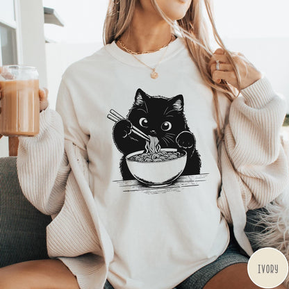 Comfort Colors tee in Ivory featuring graphic illustration of a cute black cat eating a bowl of ramen