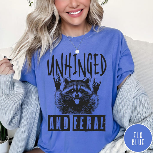 Comfort Colors tee in Flo Blue featuring graphic style raccoon with tongue out and rock and roll hands
