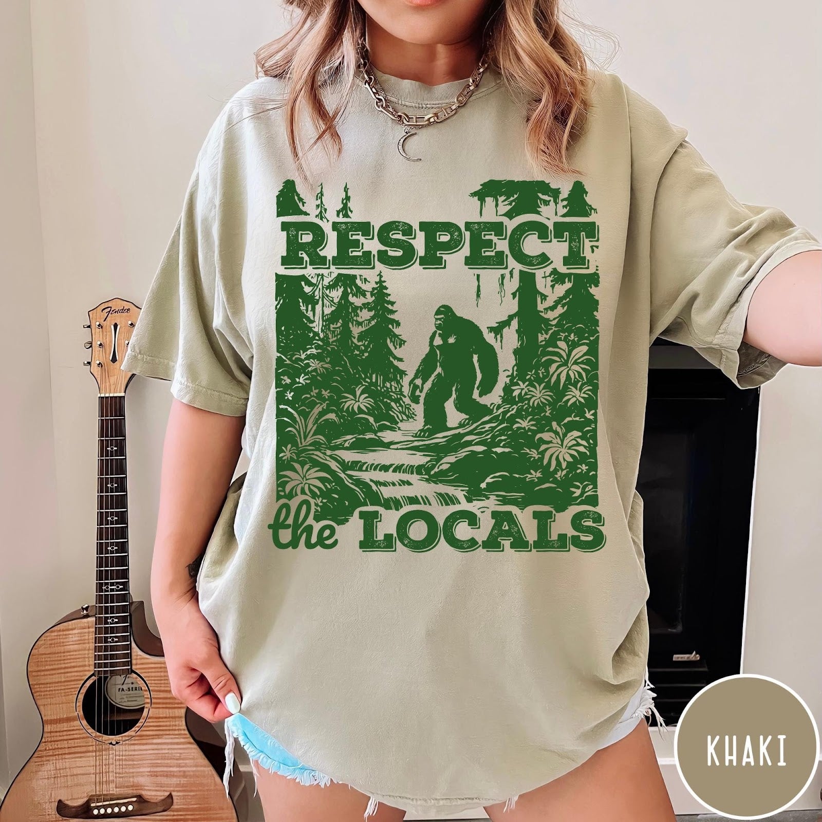 Comfort Colors tee in Khaki featuring vintage style graphic of Bigfoot walking through a forest by a river