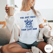 Comfort Colors tee in White featuring western style graphic of a raccoon wearing a cowboy hat