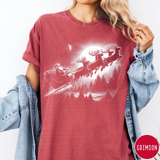 Comfort Colors tee in Crimson featuring vintage style Santa Claus flying in a sleigh with reindeer