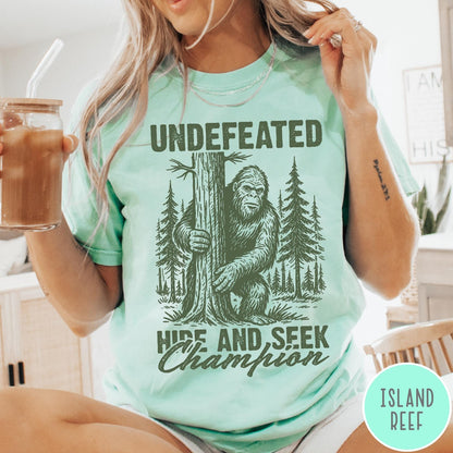 Comfort Colors tee in Island Reef featuring vintage style Bigfoot graphic hiding behind a tree in the forest