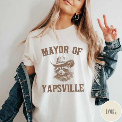 Comfort Colors tee in Ivory featuring western style graphic of a raccoon wearing a cowboy hat and bandana