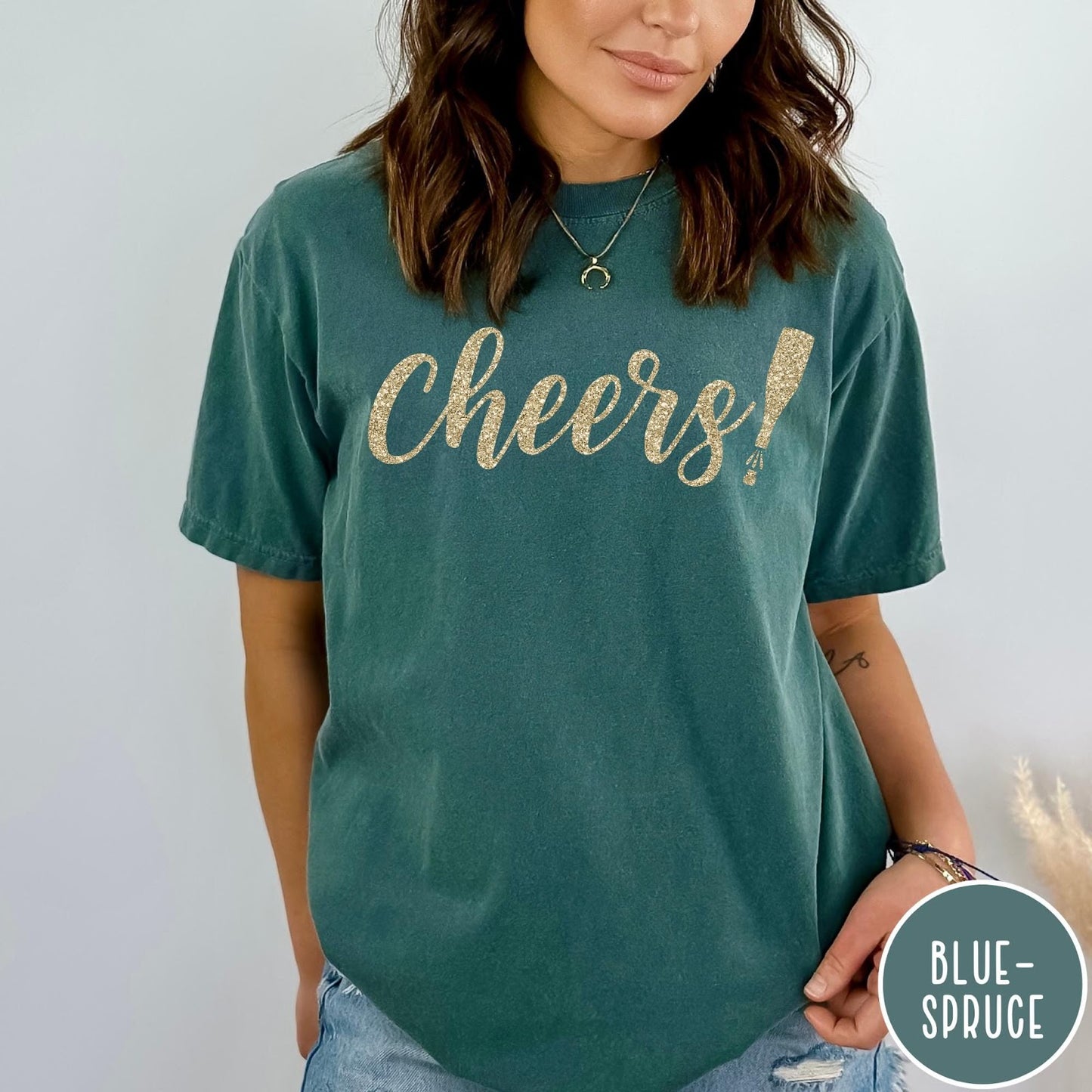 Comfort Colors tee in Blue Spruce featuring New Year celebration graphic with gold glitter cheers text and champagne bottle