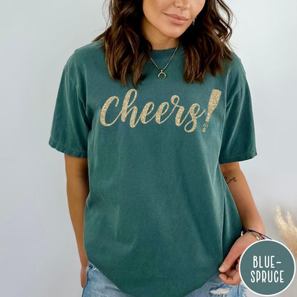 Comfort Colors tee in Blue Spruce featuring New Year celebration graphic with gold glitter cheers text and champagne bottle