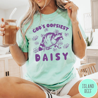 Comfort Colors tee in Island Reef featuring whimsical raccoon graphic with daisy flowers and God's Oopsiest Daisy text