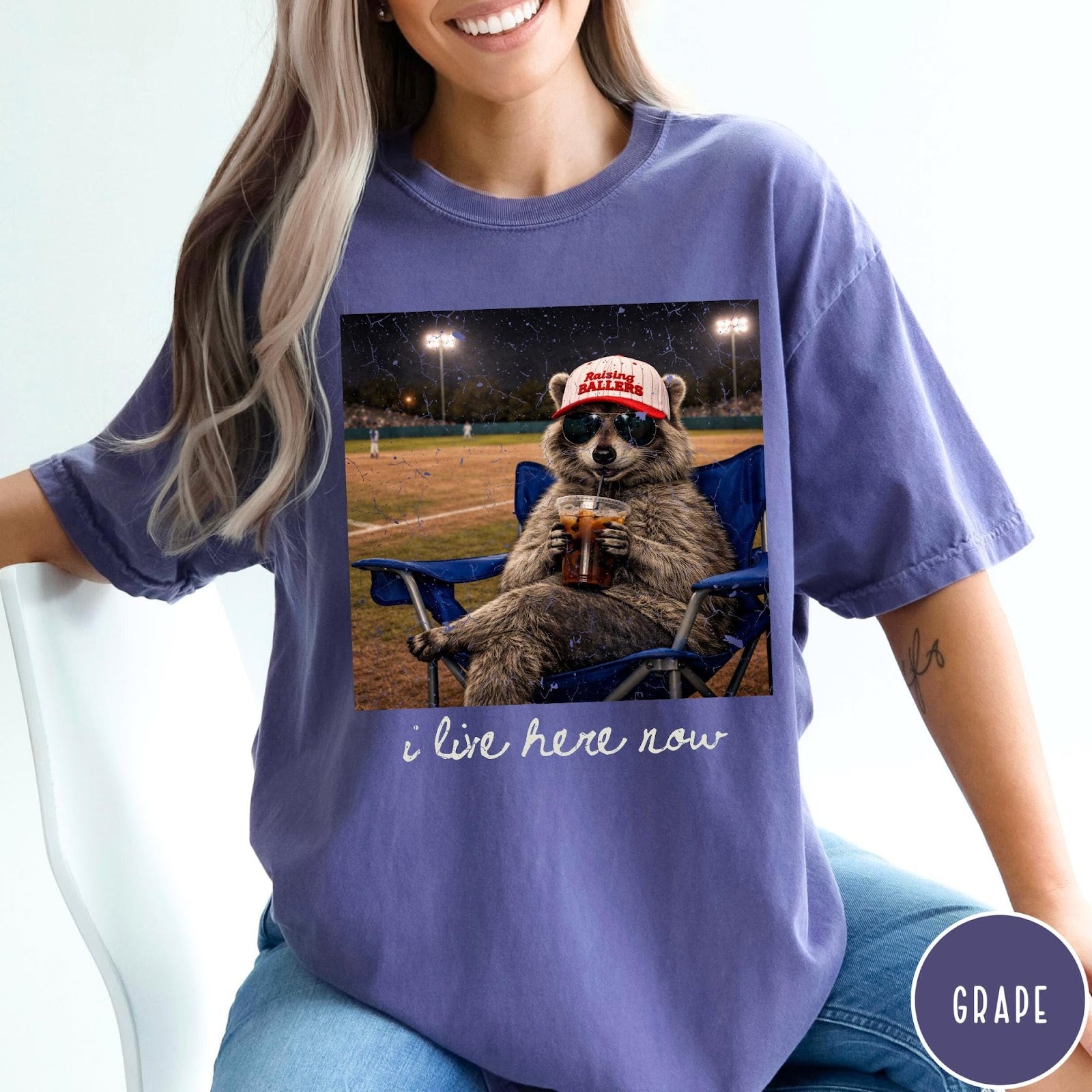 Comfort Colors tee in Grape featuring graphic raccoon wearing sunglasses and baseball cap sitting in camping chair