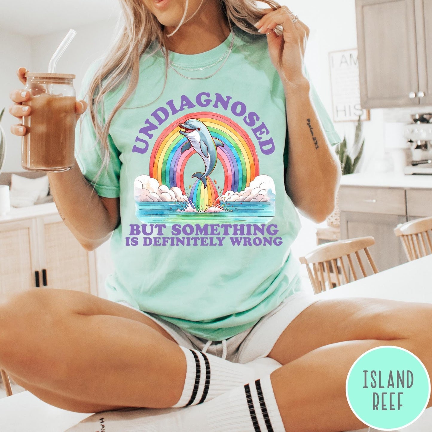 Comfort Colors tee in Island Reef featuring graphic style illustration of a dolphin jumping through a colorful rainbow