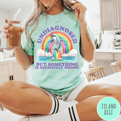Comfort Colors tee in Island Reef featuring graphic style illustration of a dolphin jumping through a colorful rainbow
