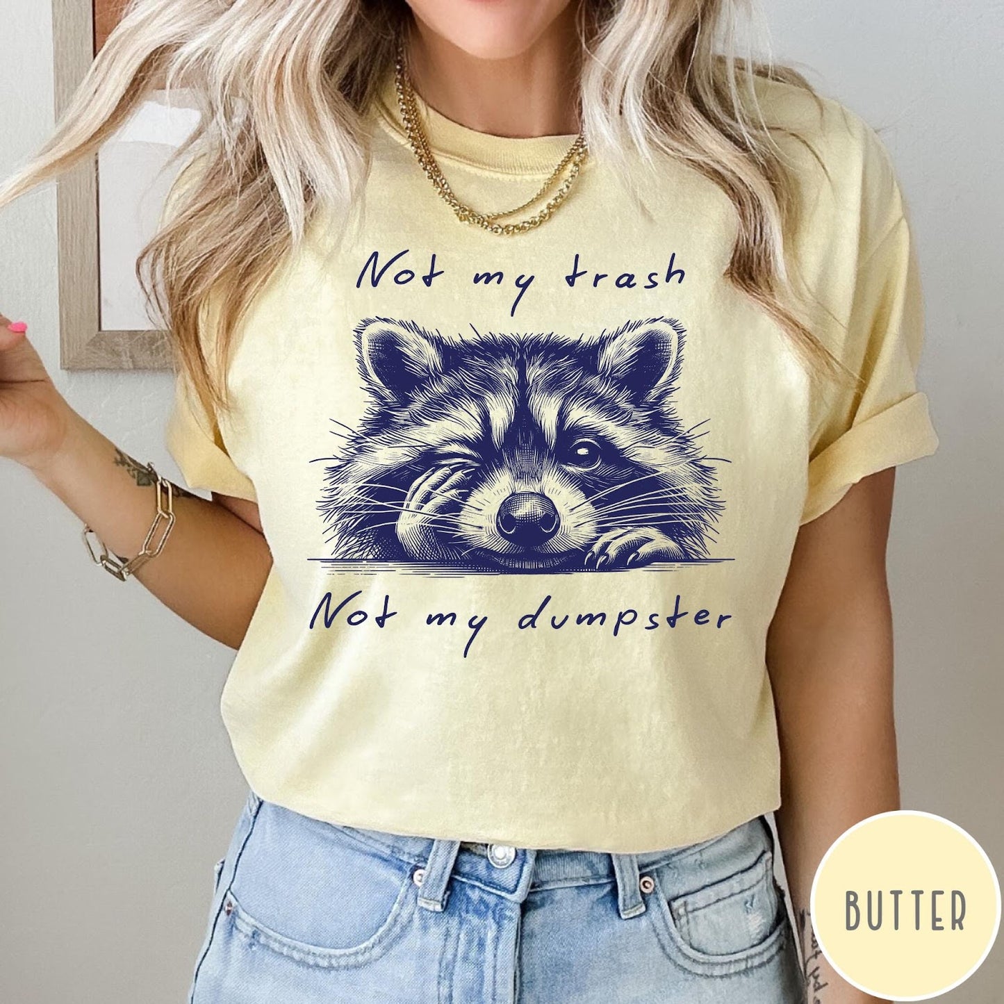 Comfort Colors tee in Butter featuring illustrated style graphic of a winking raccoon with text not my trash