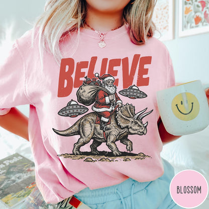 Comfort Colors tee in Blossom featuring graphic illustration of Santa riding a dinosaur with flying saucers above
