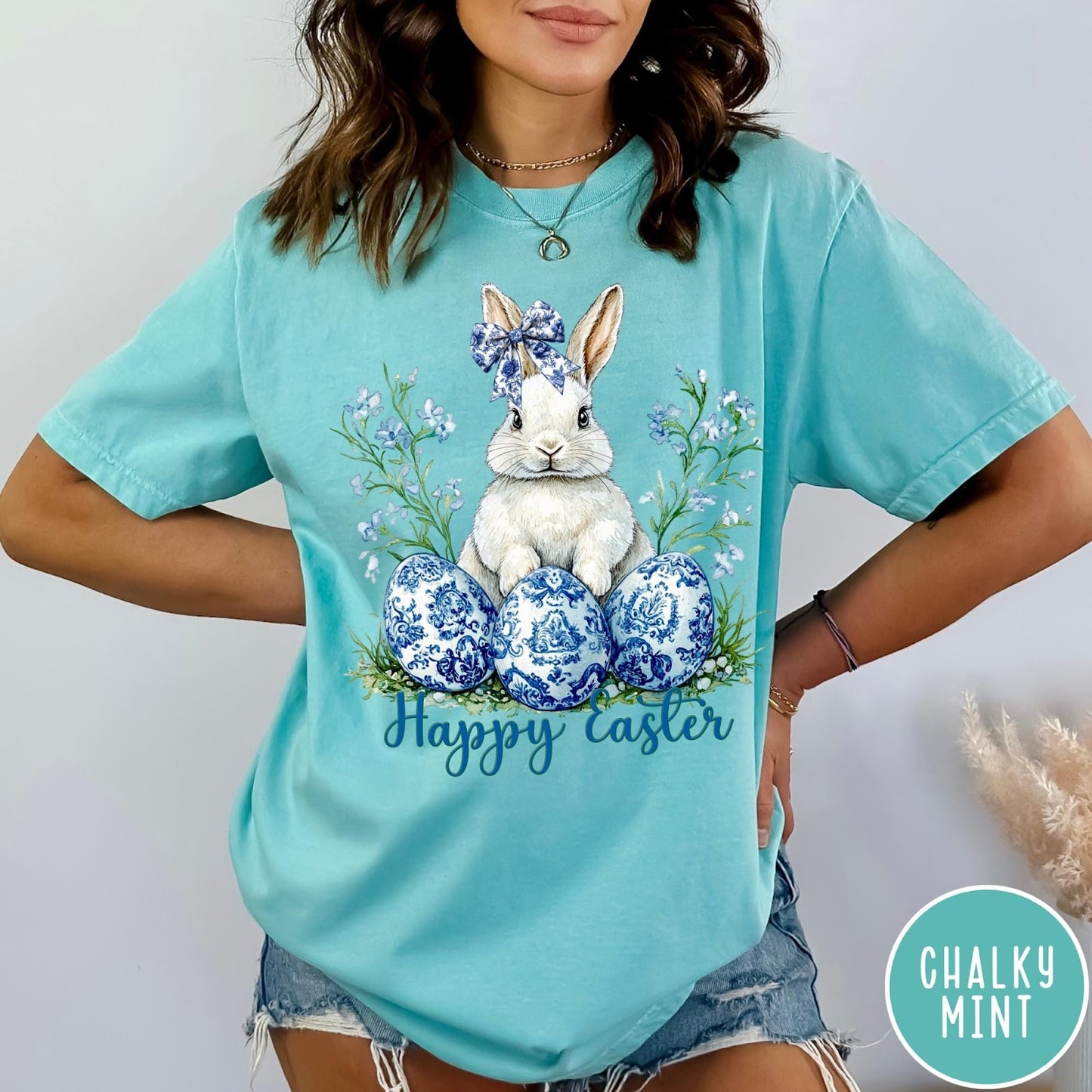 Comfort Colors tee in Chalky Mint featuring Easter bunny graphic with blue floral bow and patterned Easter eggs