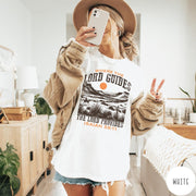 Comfort Colors tee in White featuring desert landscape graphic with a rider and sun design.