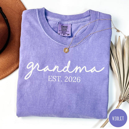 Comfort Colors tee in Violet featuring cursive Grandma Est 2026 text in a clean white graphic style