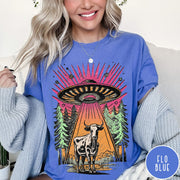 Comfort Colors tee in Flo Blue featuring graphic style cow being abducted by a UFO in the forest