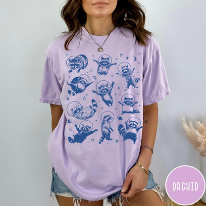 Comfort Colors tee in Orchid featuring whimsical space design with multiple raccoons wearing glass astronaut helmets and stars