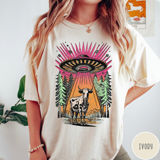 Comfort Colors tee in Ivory featuring graphic style cow being abducted by a UFO in the forest