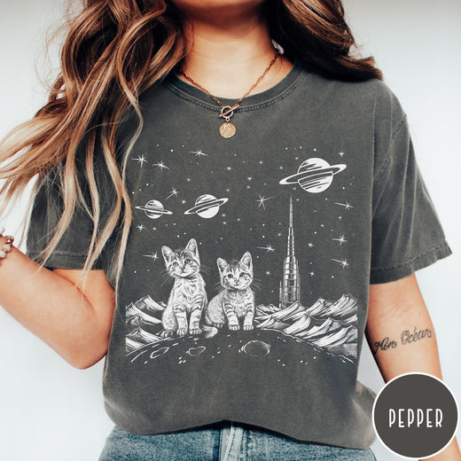 Comfort Colors tee in Pepper featuring line art graphic of two kittens sitting on a planet with rocket