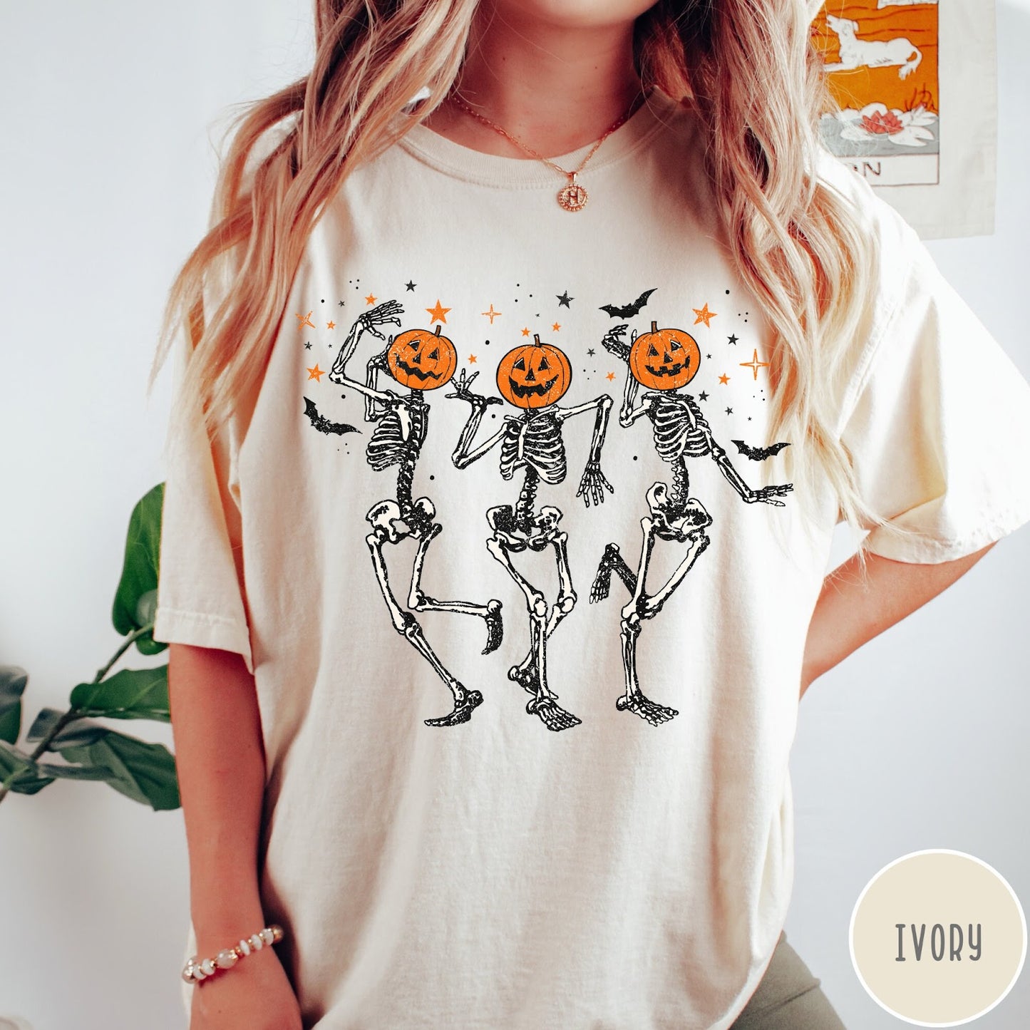 Comfort Colors tee in Ivory featuring dancing skeleton graphic with jack-o'-lantern heads and small orange stars