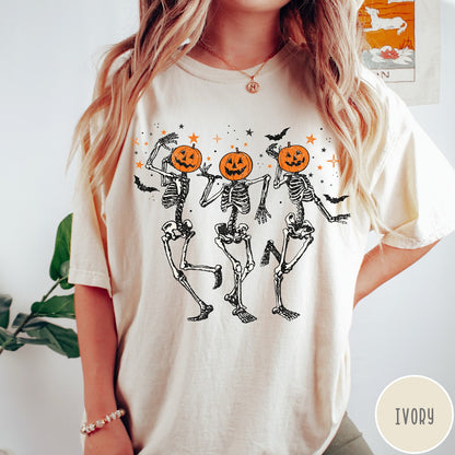 Comfort Colors tee in Ivory featuring dancing skeleton graphic with jack-o'-lantern heads and small orange stars