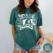Comfort Colors tee in Blue Spruce featuring graphic style illustration of a woman sleeping surrounded by horror polaroids