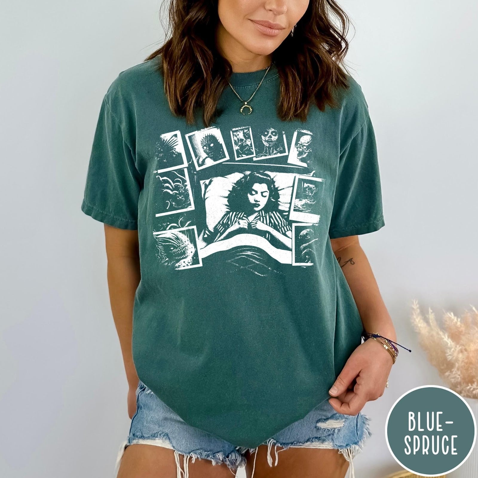 Comfort Colors tee in Blue Spruce featuring graphic style illustration of a woman sleeping surrounded by horror polaroids