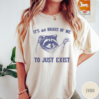 Comfort Colors tee in Ivory featuring illustrative raccoon graphic with text It's So Brave Of Me To Just Exist