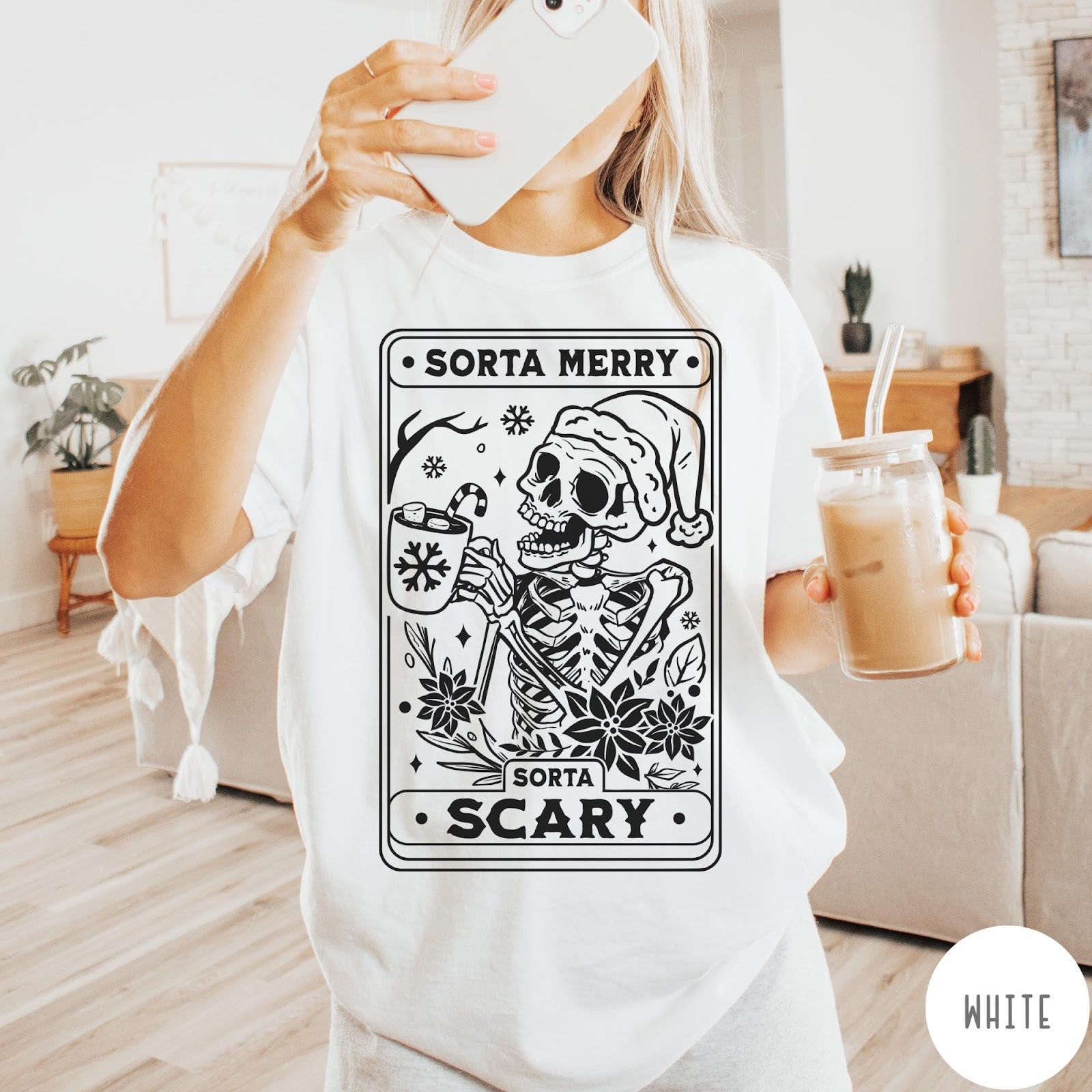 Comfort Colors tee in White featuring graphic illustration of a skeleton in a Santa hat holding cocoa