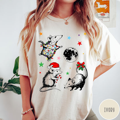 Comfort Colors tee in Ivory featuring holiday possum graphic with Christmas lights, candy cane, and moon.