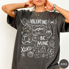 Comfort Colors tee in Pepper featuring sketch style Valentine's Day collage graphic with cupid, bear, and hearts