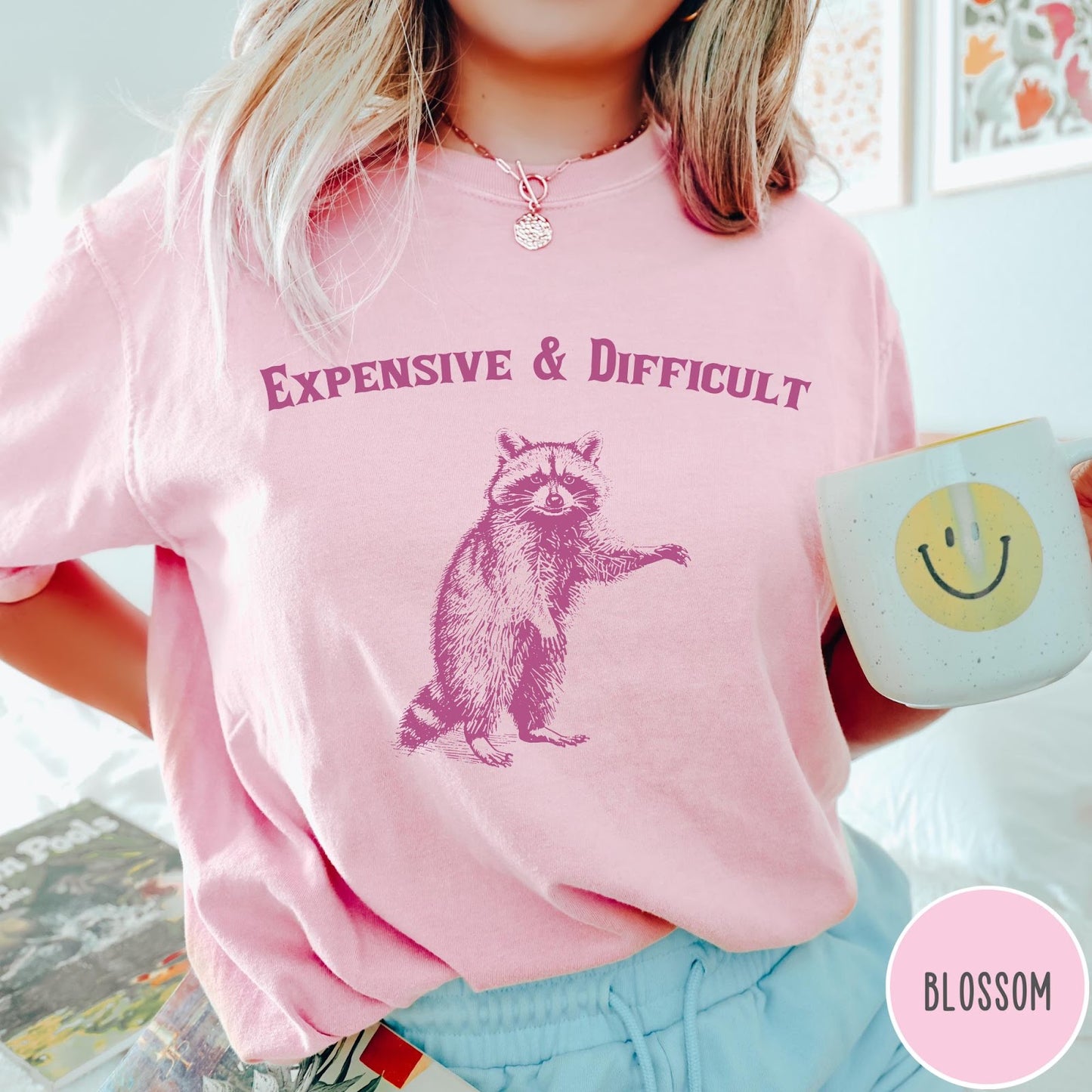 Comfort Colors tee in Blossom featuring vintage style graphic of a standing raccoon with text Expensive and Difficult
