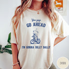 Comfort Colors tee in Ivory featuring illustration style graphic of a bear wearing a party hat riding bicycle