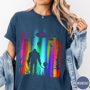 Comfort Colors tee in Midnight featuring a vibrant graphic of Bigfoot and an alien holding hands in forest