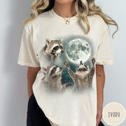 Comfort Colors tee in Ivory featuring artistic graphic of three raccoons reaching toward a bright full moon