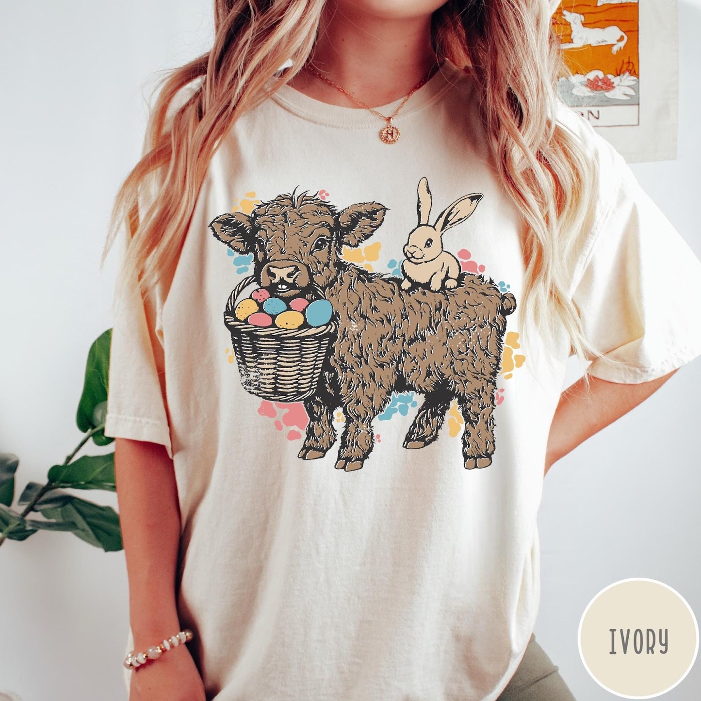 Comfort Colors tee in Ivory featuring graphic style illustration of a Highland cow with bunny and eggs