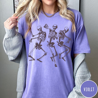 Comfort Colors tee in Violet featuring dancing skeletons graphic illustration on the front of the shirt